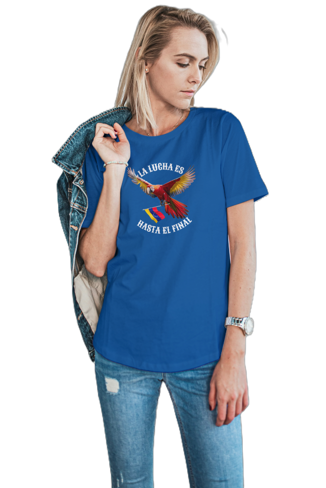 A blond woman is wearing a blue unisex t-shirt featuring a colorful macaw flying while holding the Venezuelan flag. The text "La Lucha Es" is at the top, and "Hasta El Final" is below the macaw. 
