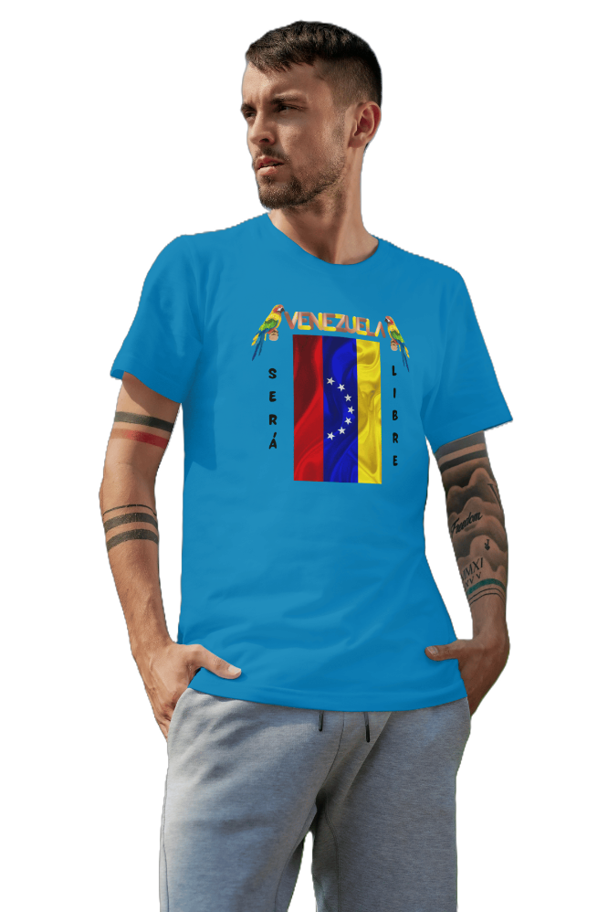 A man is wearing a blue unisex t-shirt featuring a Venezuelan flag, the name "Venezuela" at the top, and a colorful macaw on either side. The text "Será Libre" is vertically next to the flag. He's looking to the right, with both hands in his pockets.