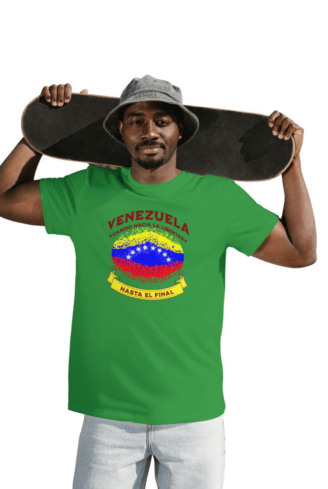 A smiling man is wearing a green unisex t-shirt featuring a colorful, elliptically shaped Venezuelan flag dotted (like an explosion), with the text "Venezuela Camino Hacia La Libertad" at the top and "Hasta El Final" on a yellow ribbon below the flag.