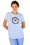 A smiling woman is wearing a light blue unisex t-shirt featuring a Venezuelan flag inside heart-shaped hands, the text "Por Venezuela Hasta El Final", and a pair of macaws on either side.