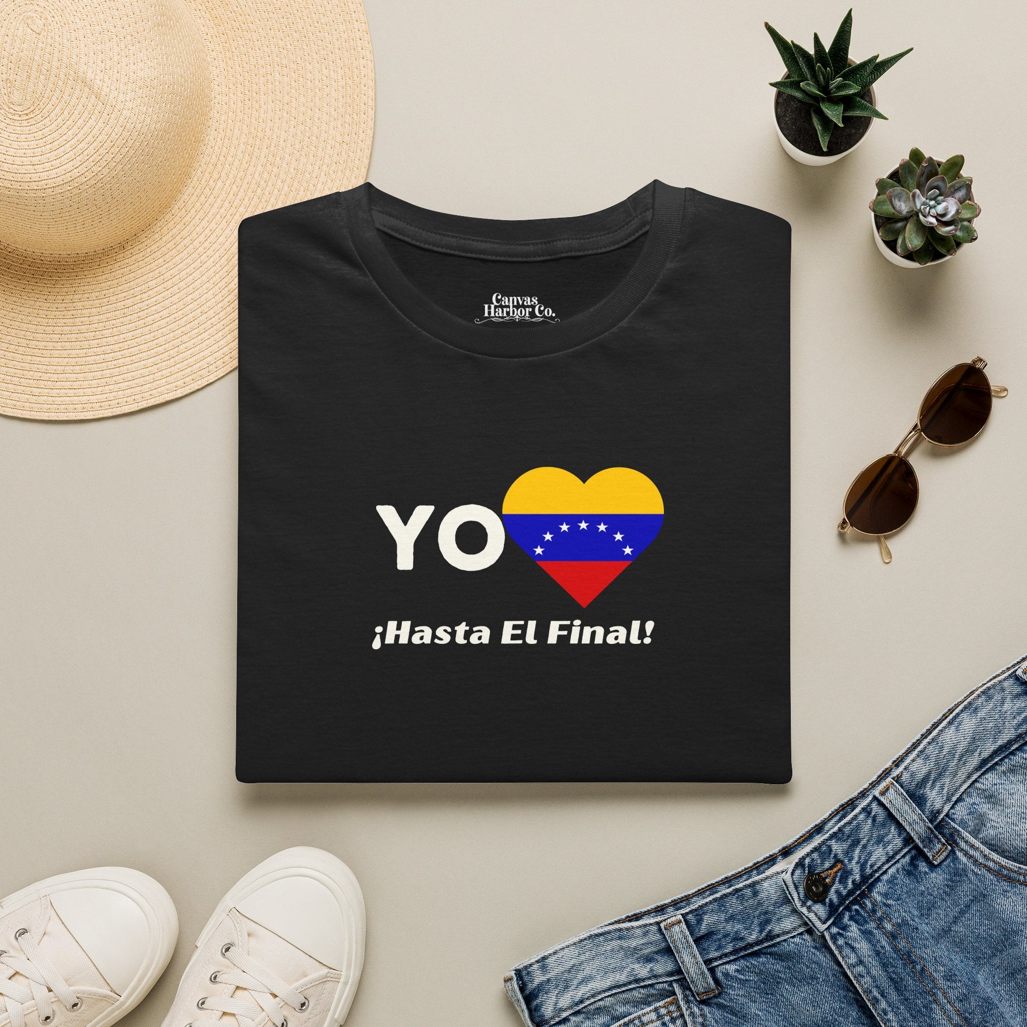 Franela negra doblada sobre una mesa, con la bandera venezolana de 7 estrellas en forma de corazón, la palabra "YO" a la izquierda y el texto "¡HASTA EL FINAL!" debajo.