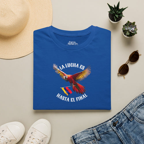 Franela azul doblada sobre una mesa, con la imagen de un guacamayo y la bandera venezolana. La frase "LA LUCHA ES HASTA EL FINAL" rodea al ave.