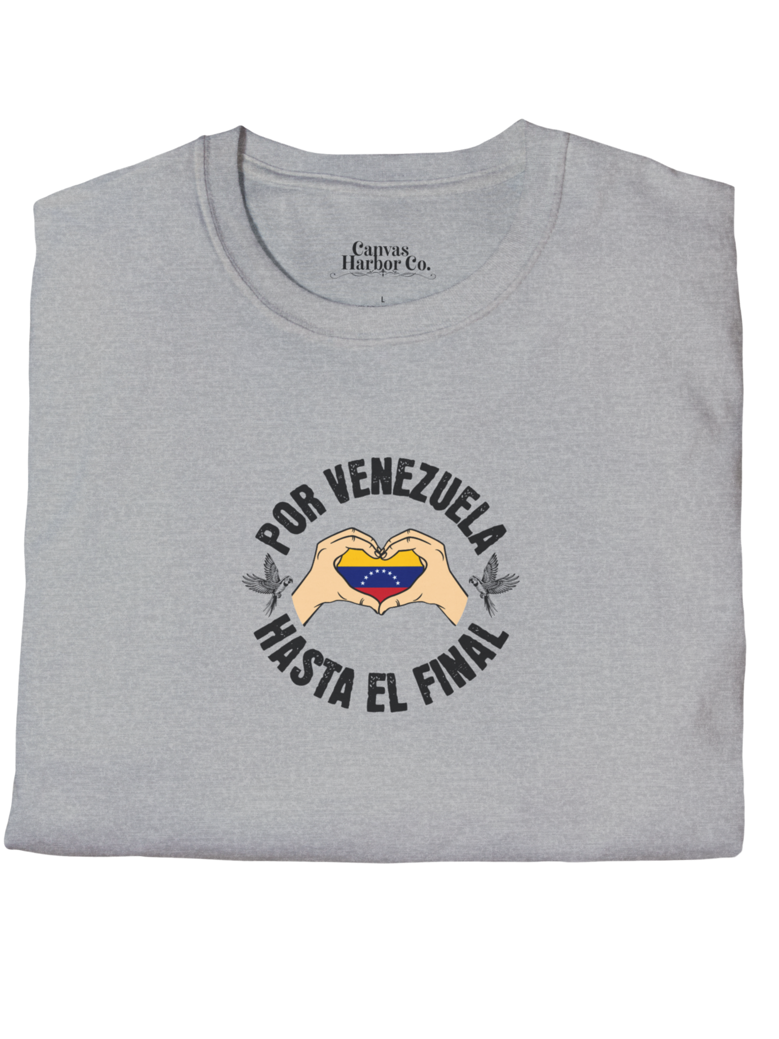 Franela doblada color gris claro, con la bandera venezolana dentro de unas manos en forma de corazón, el texto "POR VENEZUELA HASTA EL FINAL" alrededor y una guacamaya a cada lado.