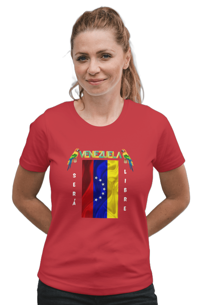 A woman is wearing a red unisex t-shirt featuring a Venezuelan flag, the name "Venezuela" at the top, and a colorful macaw on either side. The text "Será Libre" is vertically next to the flag. She smiles, both hands behind her back.