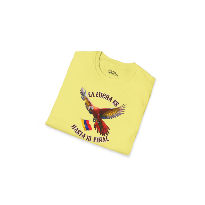 A folded pale-yellow unisex t-shirt featuring a colorful macaw flying while holding the Venezuelan flag. The text "La Lucha Es" is at the top, and "Hasta El Final" is below the macaw.