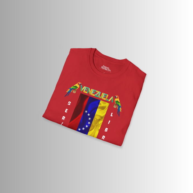 A folded red unisex t-shirt featuring a Venezuelan flag, the name "Venezuela" at the top, and a colorful macaw on either side. The words "Será" and "Libre" are vertically positioned beside the flag.