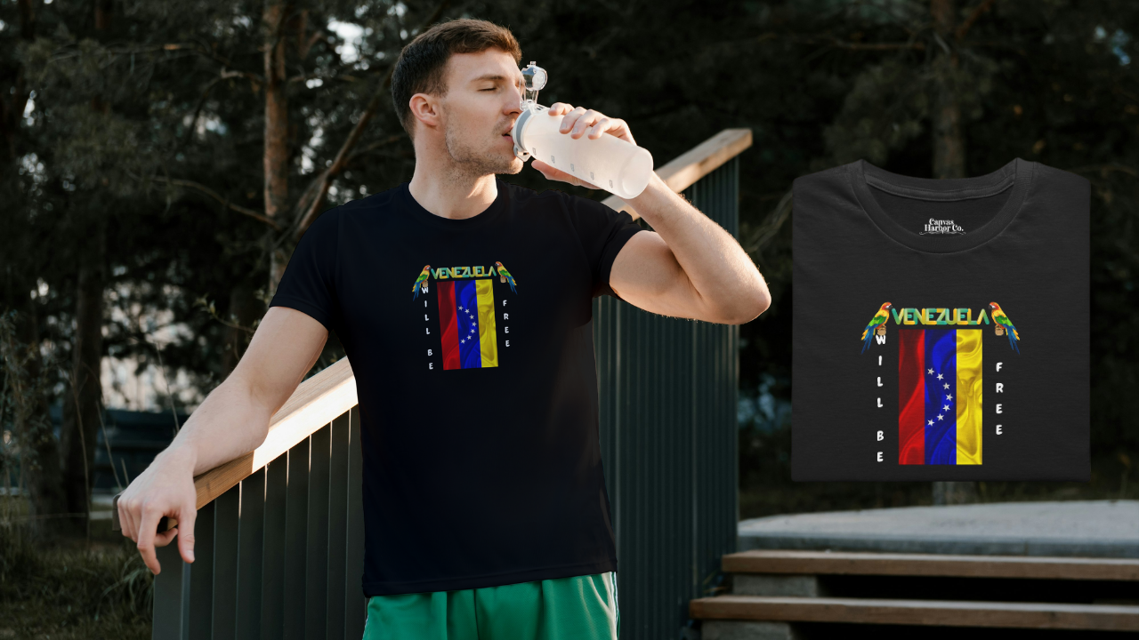Black folded T-shirt featuring the 7-star Venezuelan flag, the name VENEZUELA at the top, and one macaw on each side. The words WILL BE and FREE are all placed vertically next to the flag. 
On the left, a young man is wearing the T-shirt. He’s standing, drinking some water.