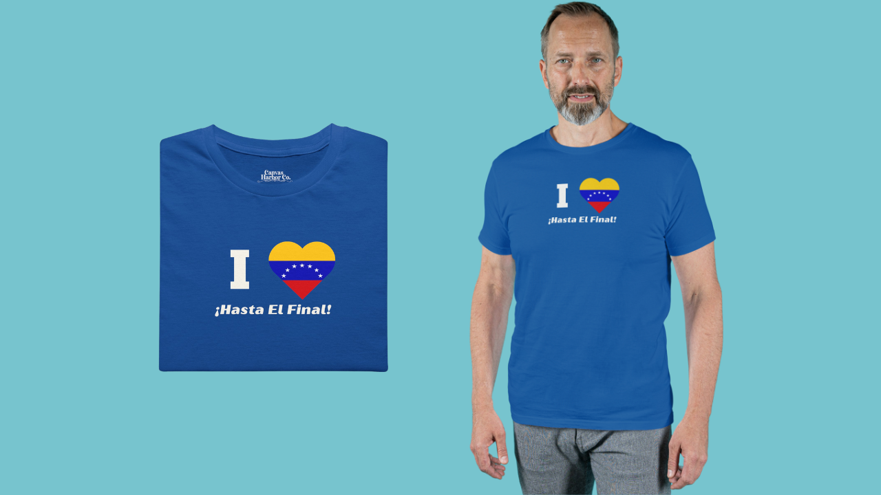 Blue folded T-shirt featuring the 7-star Venezuelan flag in the shape of a heart, the word "I" on the left, and the text "¡HASTA EL FINAL!" below.
On the right, a man wears the T-shirt. He’s standing, facing forward.