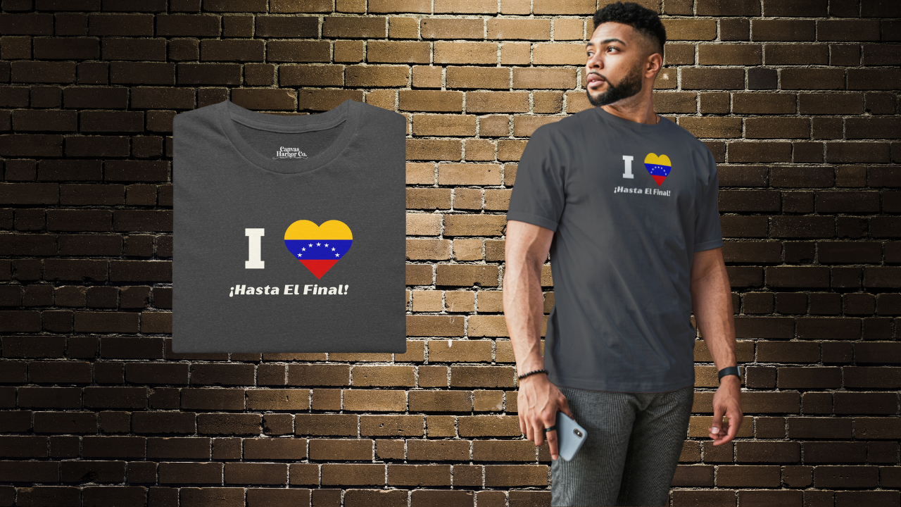 Dark gray folded T-shirt featuring the 7-star Venezuelan flag in the shape of a heart, the word "I" on the left, and the text "¡HASTA EL FINAL!" below.
On the right, an Afro-American man wears the T-shirt. He’s standing, looking to his right.