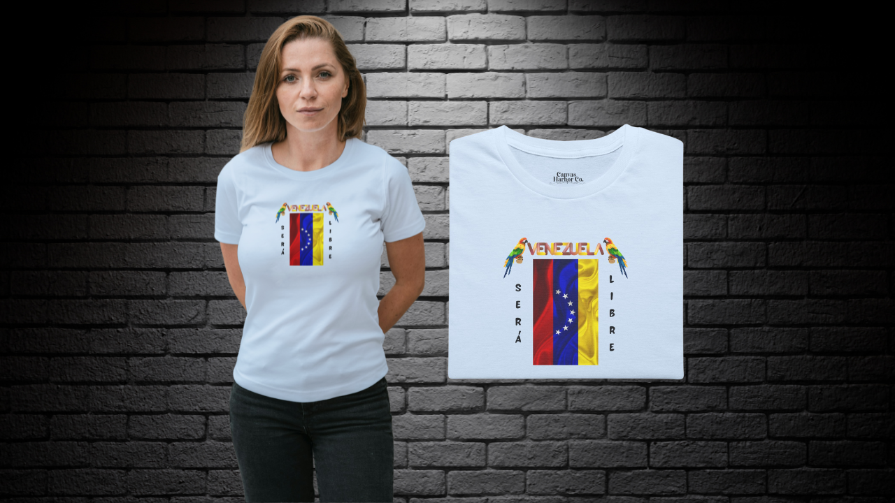 Franela doblada color azul claro con la bandera venezolana de 7 estrellas, el nombre VENEZUELA arriba y una guacamaya a cada lado. Las palabras SERÁ y LIBRE se ubican verticalmente junto a la bandera.
A la izquierda, hay una mujer joven que viste la franela. Ella está de pie, con ambas manos detrás de su espalda. 