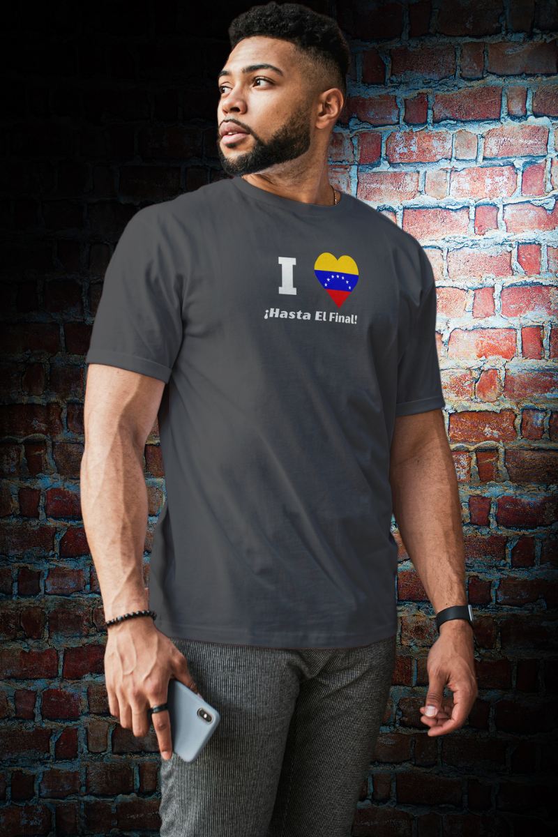 An Afro-American man wears a dark gray T-shirt featuring the 7-star Venezuelan flag in the shape of a heart, the word "I" on the left, and the text "¡HASTA EL FINAL!" below.
He’s standing, looking to his right.