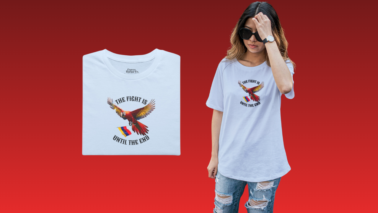 Light blue folded T-shirt featuring an image of a macaw and the Venezuelan flag. The text "THE FIGHT IS UNTIL THE END" surrounds the bird.
On the right, a young woman wears the T-shirt. She’s standing, wearing sunglasses.