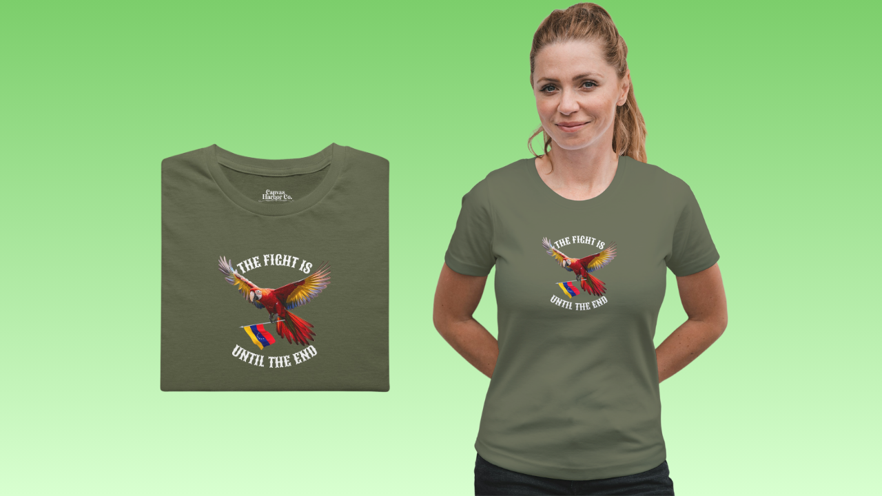 Olive green folded T-shirt featuring an image of a macaw and the Venezuelan flag. The text "THE FIGHT IS UNTIL THE END" surrounds the bird.
On the right, a blonde smiling woman wears the T-shirt. She’s standing, holding her hands behind her back.