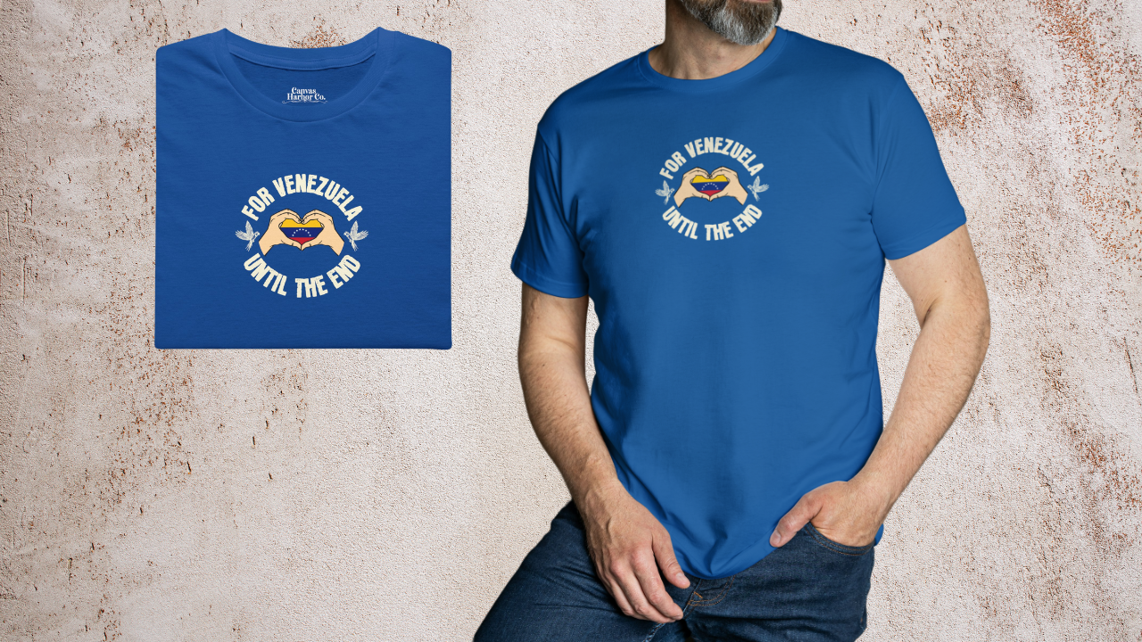 Blue folded T-shirt featuring the Venezuelan flag inside heart-shaped hands, the text “FOR VENEZUELA UNTIL THE END” around it, and one macaw on each side.
On the right, a man wears the T-shirt. He’s standing, with his left hand in his pants pocket.