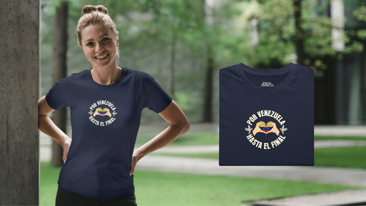 Franela color azul marino, doblada, con la bandera venezolana dentro de unas manos en forma de corazón, el texto "POR VENEZUELA HASTA EL FINAL" alrededor y una guacamaya a cada lado.
A la izquierda, una mujer rubia viste la franela. Ella está en un parque, sonriendo y mirando al frente.