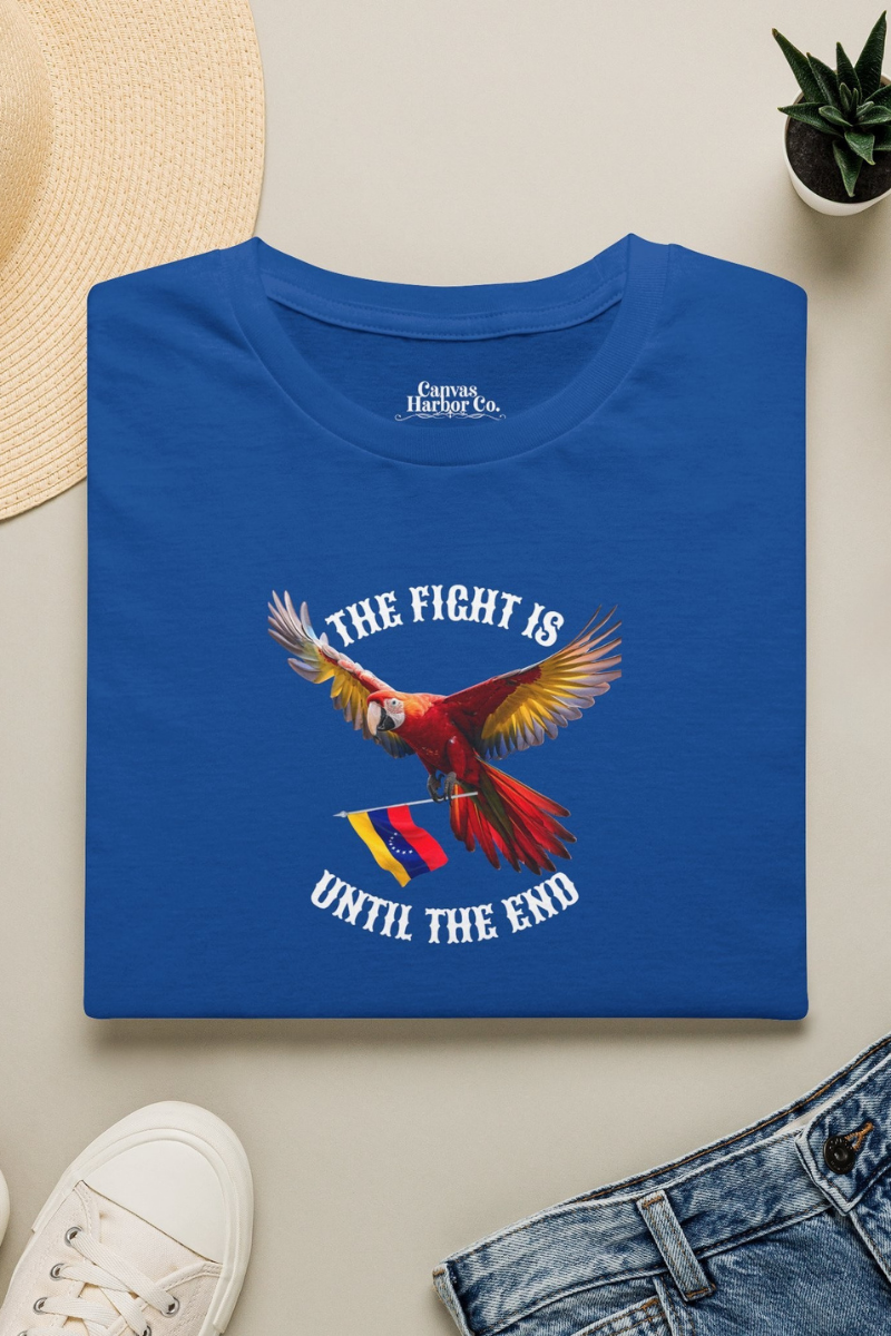 Blue folded T-shirt featuring an image of a macaw and the Venezuelan flag. The text "THE FIGHT IS UNTIL THE END" surrounds the bird.