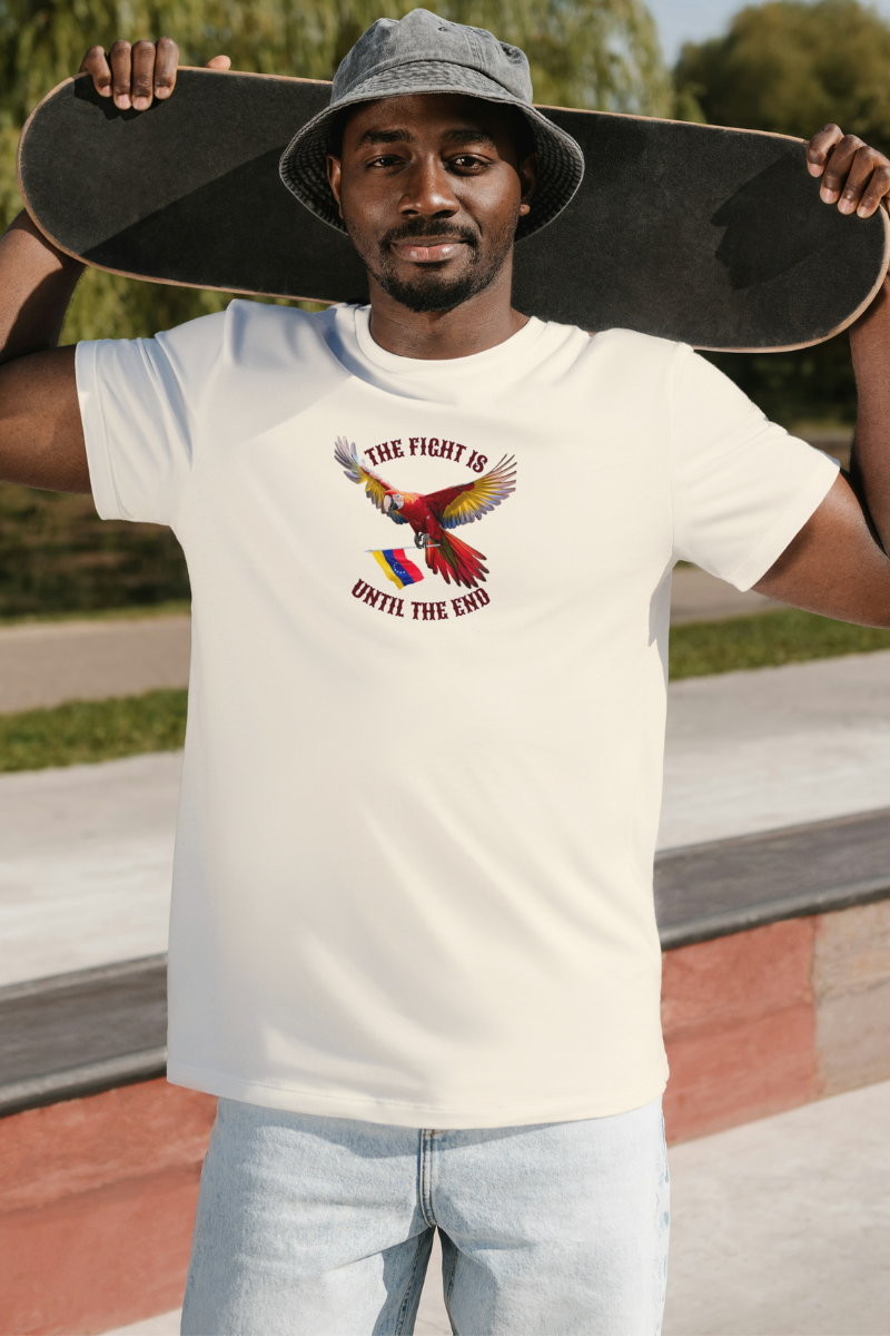 An Afro-American man wears a pale orange T-shirt featuring an image of a macaw and the Venezuelan flag. The text "THE FIGHT IS UNTIL THE END" surrounds the bird.
He’s standing, holding his skateboard behind his head.