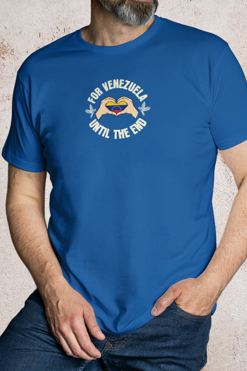 A man wears a blue T-shirt featuring the Venezuelan flag inside heart-shaped hands, the text “FOR VENEZUELA UNTIL THE END” around it, and one macaw on each side.
He’s standing, with his left hand in his pants pocket.