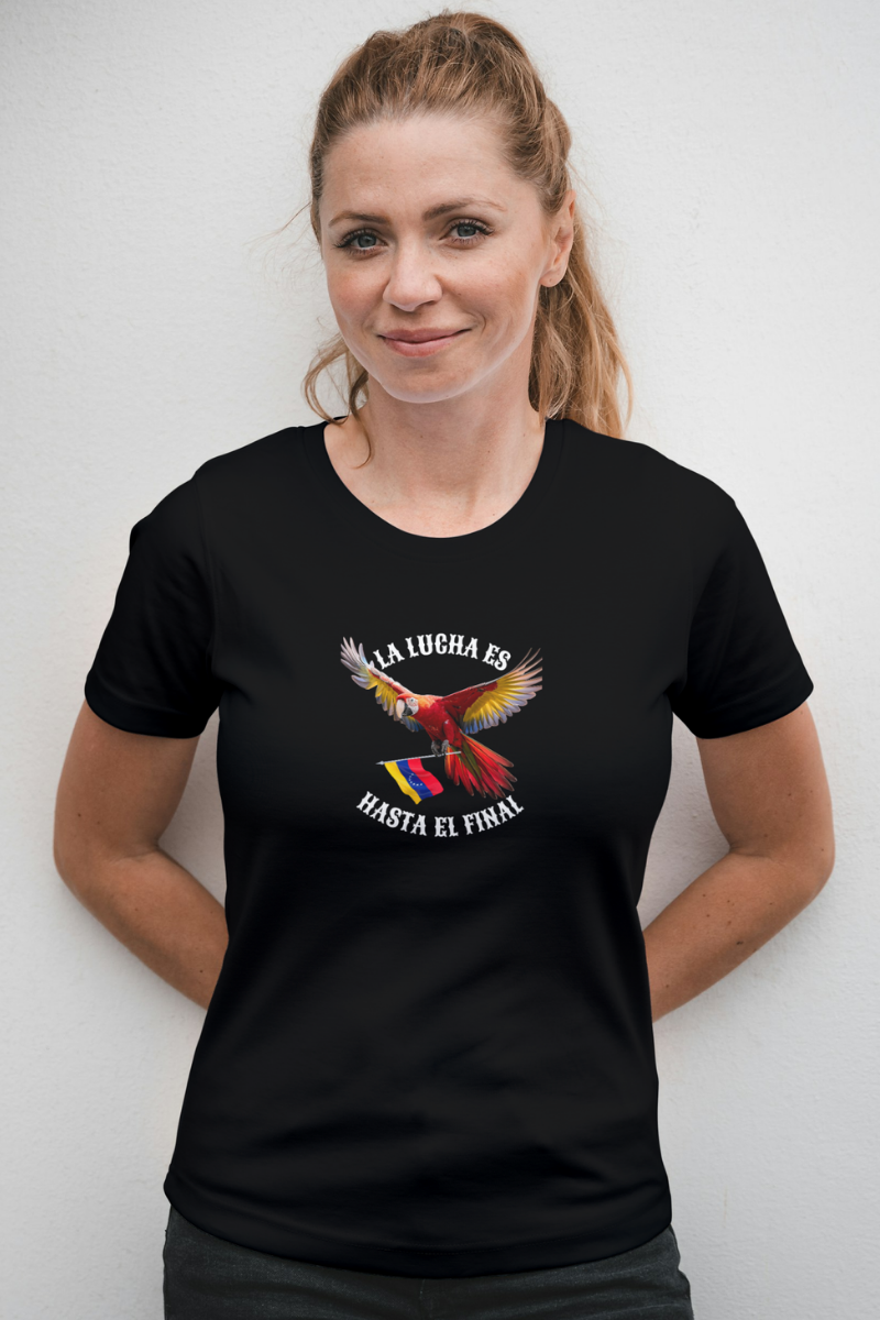 Una mujer rubia viste una franela negra con la imagen de un guacamayo con la bandera venezolana. La frase "LA LUCHA ES HASTA EL FINAL" rodea al ave.
Ella está parada, mirando al frente.