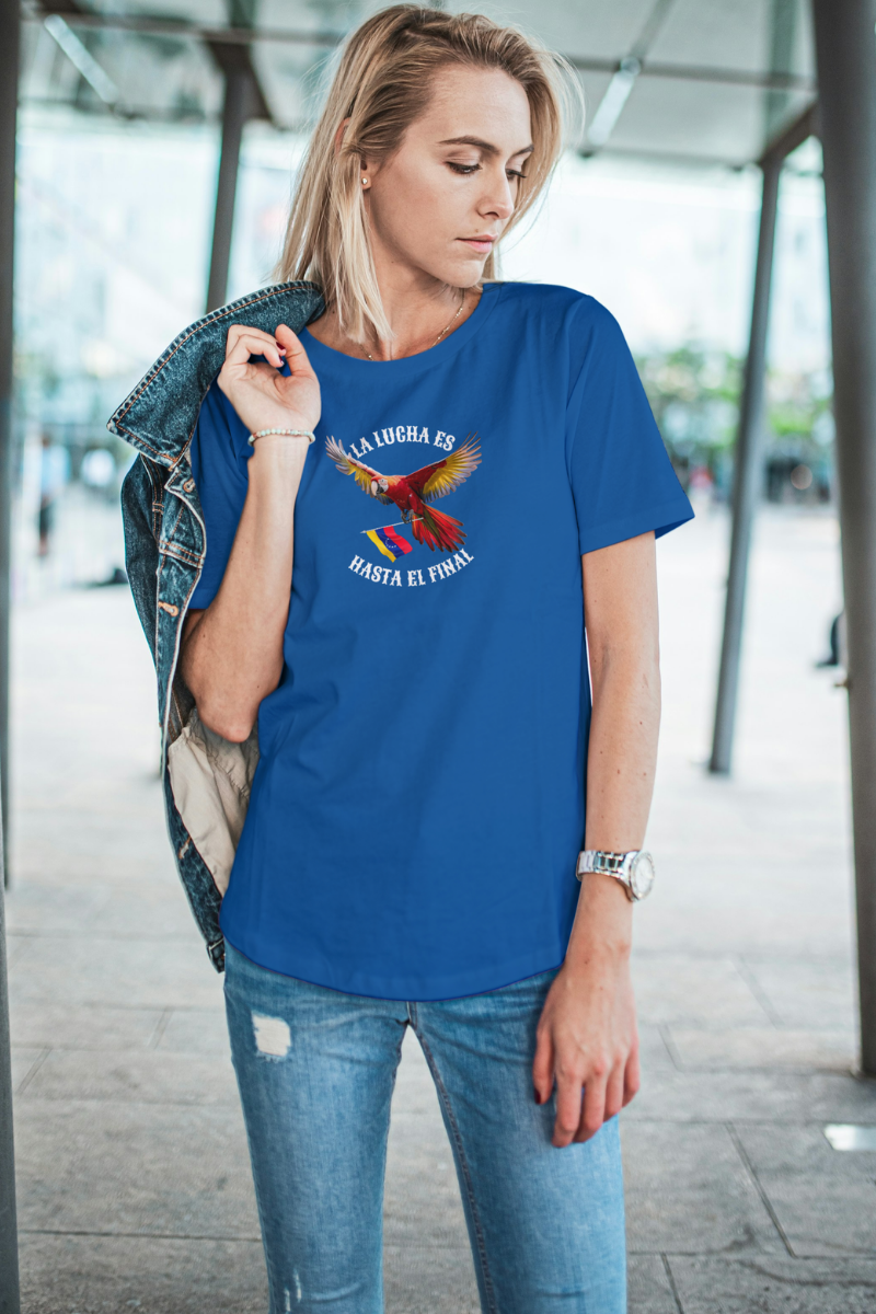 Una mujer rubia viste una franela azul con la imagen de un guacamayo con la bandera venezolana. La frase "LA LUCHA ES HASTA EL FINAL" rodea al ave.
Ella está parada, mirando por encima de su hombro izquierdo.