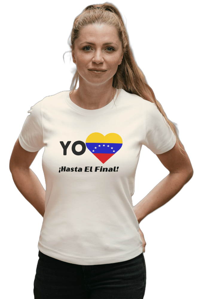 A woman is wearing a white unisex t-shirt featuring a heart-shaped Venezuelan flag, the word "Yo" on the left, and the text "¡Hasta El Final!" reading below. She is standing with her hands on her hips.