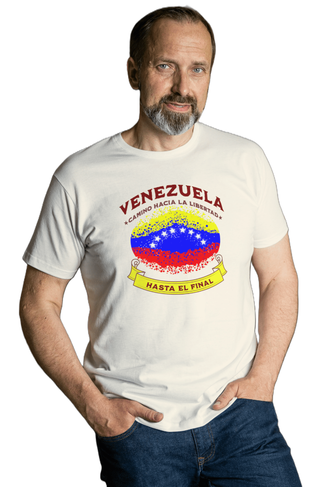 A bearded man wears a white unisex t-shirt featuring a colorful, elliptically shaped Venezuelan flag dotted (like an explosion), with the text "Venezuela Camino Hacia La Libertad" at the top and "Hasta El Final" on a yellow ribbon below the flag.