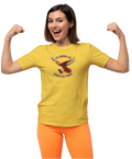 A woman is wearing a yellow unisex t-shirt featuring a colorful macaw flying while holding the Venezuelan flag. The text "La Lucha Es" is at the top, and "Hasta El Final" is below the macaw. She's smiling and flexing her arms in victory.