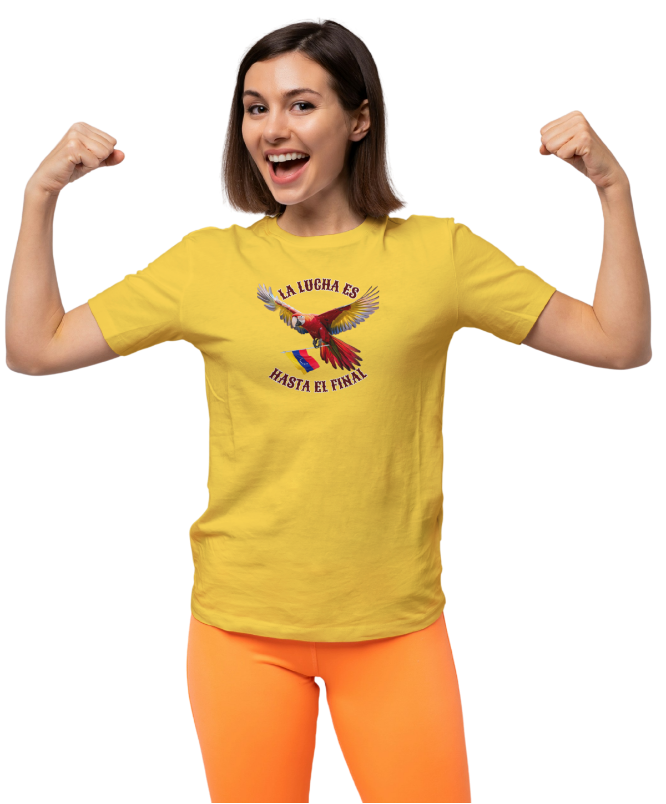 A woman is wearing a yellow unisex t-shirt featuring a colorful macaw flying while holding the Venezuelan flag. The text "La Lucha Es" is at the top, and "Hasta El Final" is below the macaw. She's smiling and flexing her arms in victory.